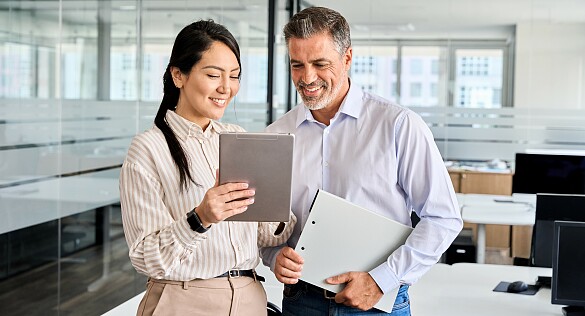 Zwei Personen stehen in einem Büro und schauen auf ein Tablet.