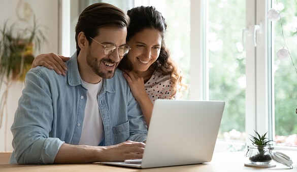 Ein Mann und eine Frau sitzen lächelnd vor einem Laptop.