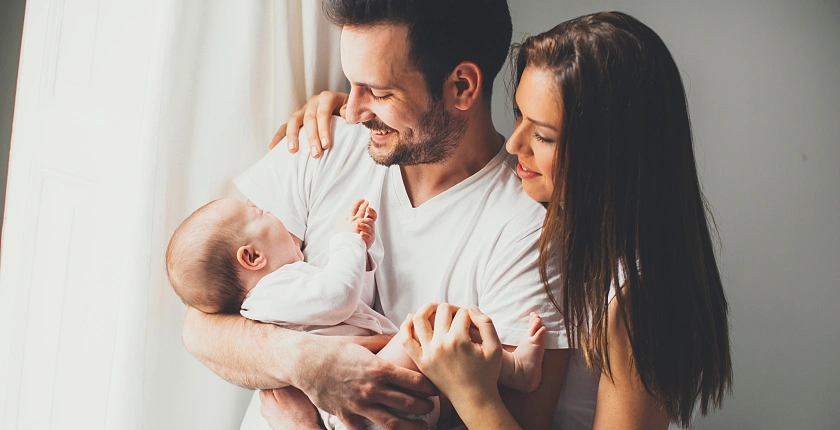 Ein Mann und eine Frau, die ein Baby im Arm des Mannes anlächeln
