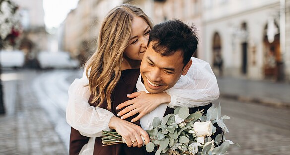 Ein Mann im Anzug trägt eine Frau im Hochzeitskleid auf dem Rücken.