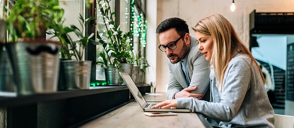 Zwei Personen sitzen an einem Laptop in einem Büro