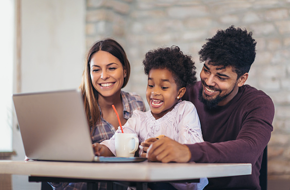 Eine Familie sitzt an einem Tisch, vor ihnen ein Laptop.