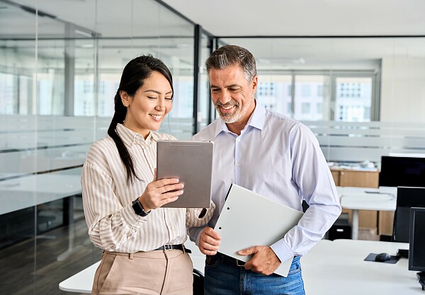 Zwei Personen schauen in einem Büro auf ein Tablet.