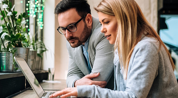 Zwei Personen sitzen an einem Laptop in einem Büro