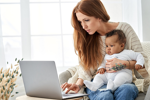 Eine Frau mit einem Kind auf dem Arm schaut auf einen Computer