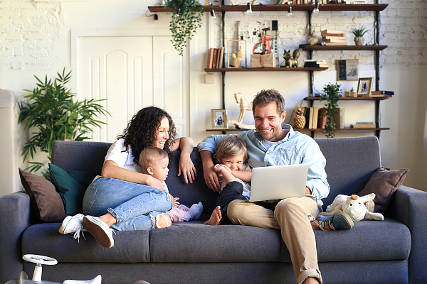 Eine vierköpfige Familie sitzt auf einem Sofa und schaut auf einen Computer