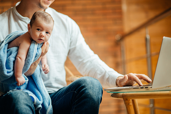 Ein Baby, das von einem Mann gehalten wird, der vor einem Computer sitzt.